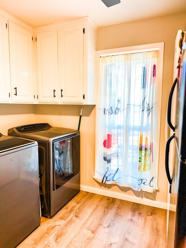 clothes washing area featuring separate washer and dryer, cabinets, and light wood-type flooring