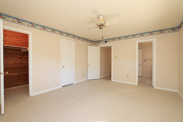 unfurnished bedroom with wood walls, light carpet, ensuite bathroom, ceiling fan, and a closet