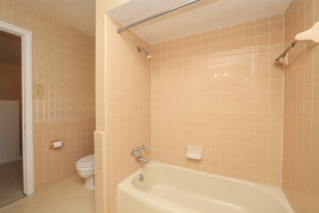 bathroom featuring tile patterned floors, tiled shower / bath combo, toilet, and tile walls