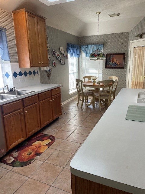 kitchen featuring pendant lighting, lofted ceiling, sink, decorative backsplash, and light tile patterned floors