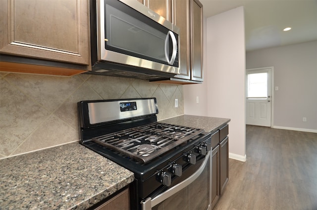 kitchen featuring dark stone countertops, decorative backsplash, stainless steel appliances, and wood-type flooring