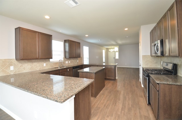 kitchen featuring light stone countertops, a center island, sink, kitchen peninsula, and appliances with stainless steel finishes