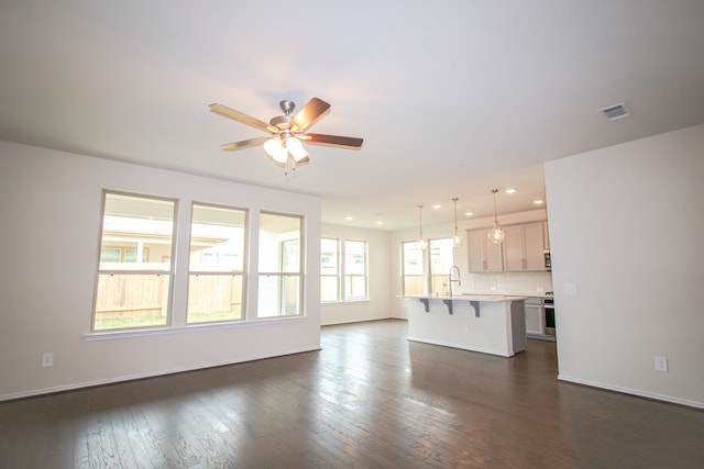 unfurnished living room with ceiling fan, sink, and dark wood-type flooring