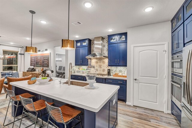 kitchen featuring stainless steel oven, wall chimney range hood, blue cabinetry, decorative light fixtures, and a breakfast bar area