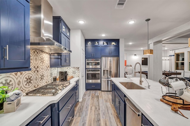 kitchen with sink, wall chimney exhaust hood, light wood-type flooring, blue cabinetry, and stainless steel appliances