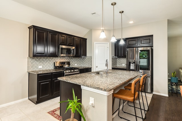 kitchen with a kitchen island with sink, sink, light wood-type flooring, light stone counters, and stainless steel appliances