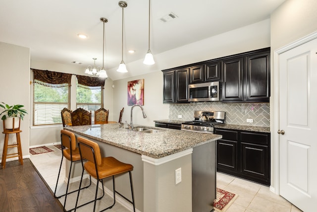 kitchen with light stone countertops, appliances with stainless steel finishes, light wood-type flooring, a kitchen island with sink, and sink