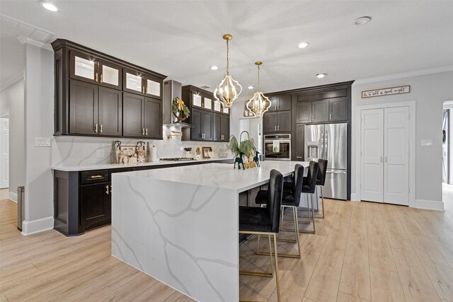 kitchen with appliances with stainless steel finishes, a kitchen island with sink, crown molding, wall chimney range hood, and decorative light fixtures