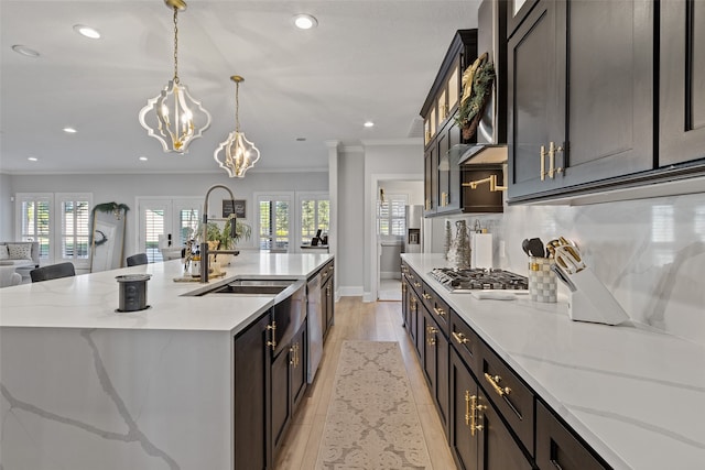 kitchen with light stone counters, an island with sink, pendant lighting, and light wood-type flooring