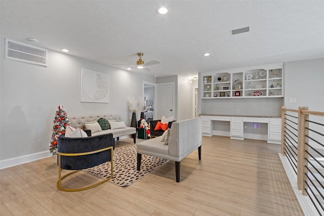 living room with ceiling fan, built in desk, and light wood-type flooring