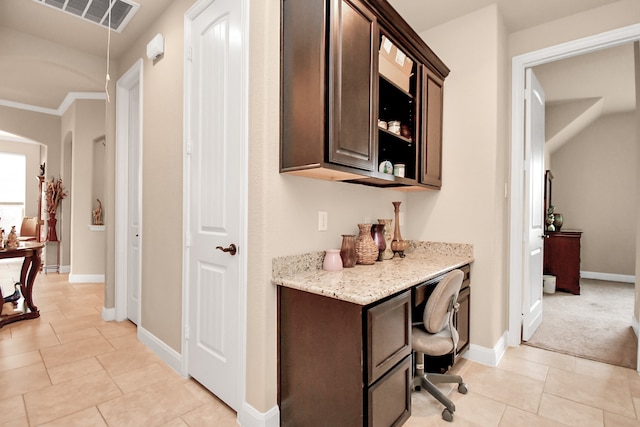 bar with light stone countertops, dark brown cabinetry, ornamental molding, and light tile patterned floors