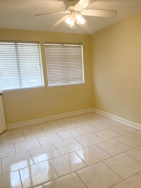 empty room with ceiling fan, light tile patterned floors, and a textured ceiling