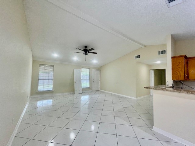 empty room featuring a textured ceiling, ceiling fan, crown molding, light tile patterned floors, and vaulted ceiling with beams