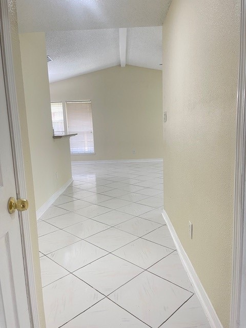 corridor with a textured ceiling and vaulted ceiling with beams