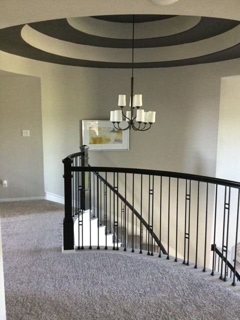 stairway featuring a tray ceiling, carpet floors, a high ceiling, and an inviting chandelier