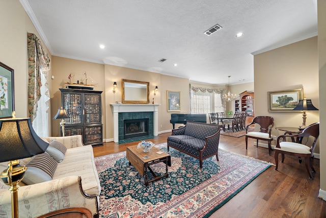 living room featuring an inviting chandelier, crown molding, hardwood / wood-style flooring, a textured ceiling, and a tiled fireplace