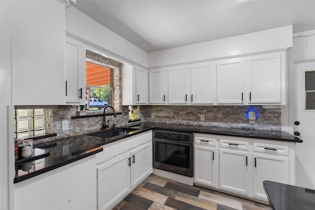 kitchen with sink, white cabinetry, dark stone countertops, and stainless steel oven