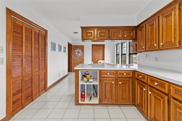 kitchen with light tile patterned floors, visible vents, brown cabinetry, a peninsula, and light countertops