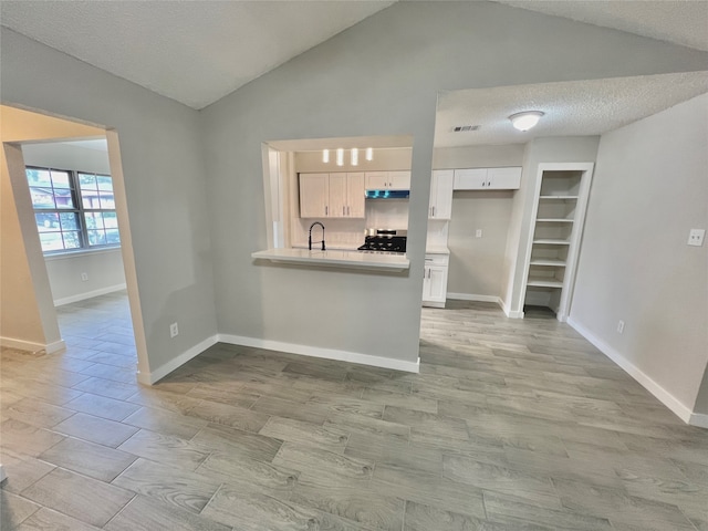 kitchen featuring white cabinets, lofted ceiling, a textured ceiling, and stainless steel range