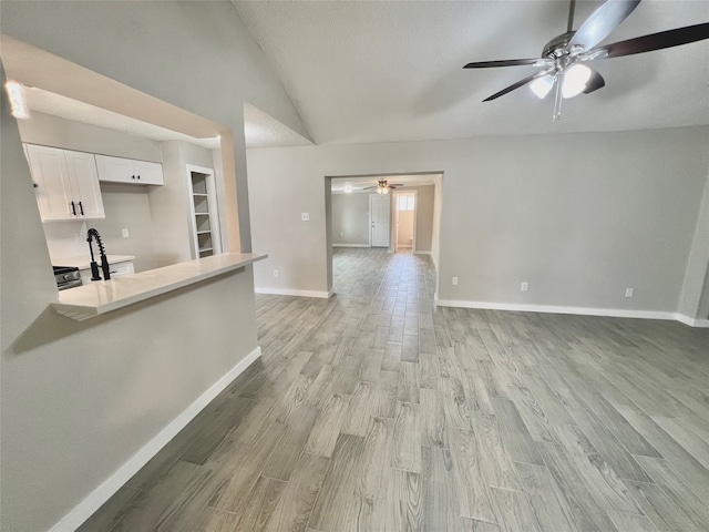 kitchen featuring ceiling fan, white cabinets, light hardwood / wood-style floors, and lofted ceiling