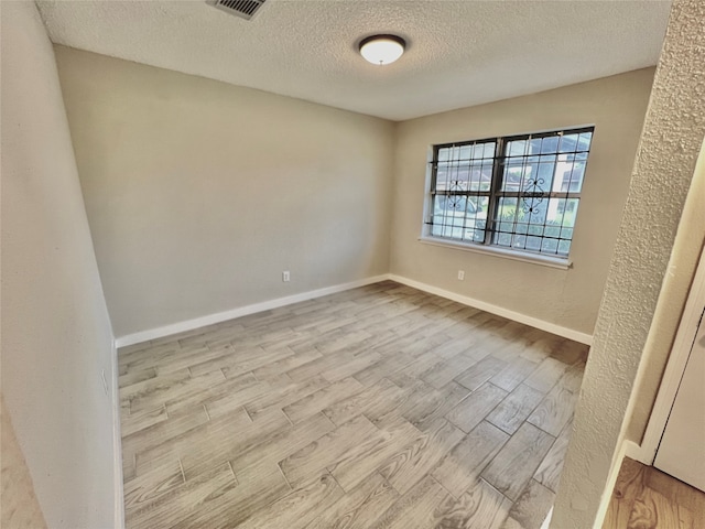 spare room featuring a textured ceiling and light hardwood / wood-style flooring