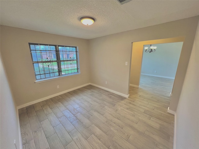 empty room with a notable chandelier, a textured ceiling, and light hardwood / wood-style flooring