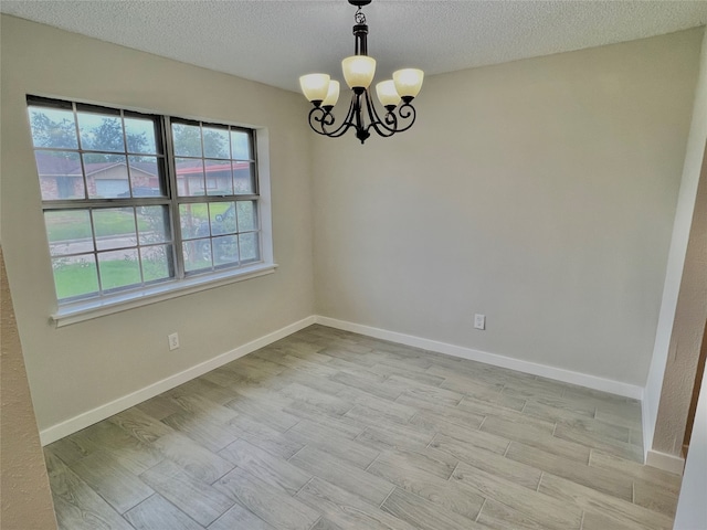 empty room featuring light hardwood / wood-style flooring, a textured ceiling, and a notable chandelier