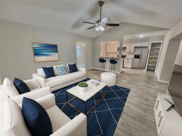 living room with a textured ceiling, sink, light hardwood / wood-style floors, and lofted ceiling