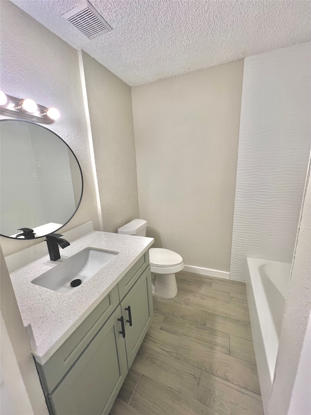 bathroom with vanity, a textured ceiling, hardwood / wood-style floors, toilet, and a tub