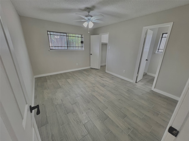 unfurnished bedroom featuring ceiling fan, light hardwood / wood-style floors, a spacious closet, and a textured ceiling