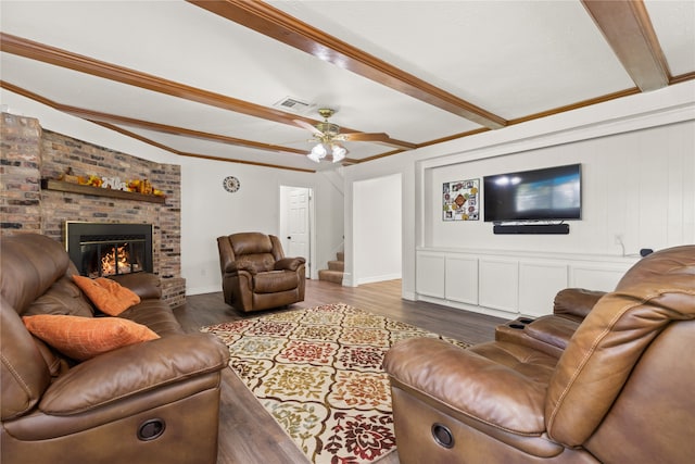 living room featuring dark hardwood / wood-style flooring, a brick fireplace, ornamental molding, ceiling fan, and beamed ceiling