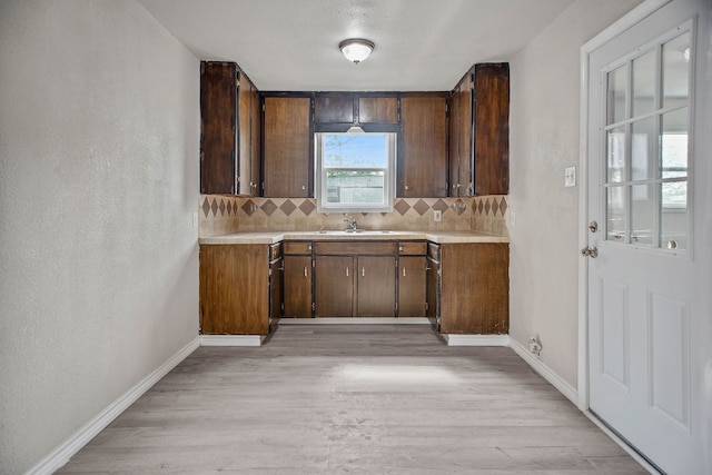 kitchen featuring dark brown cabinets, light wood-type flooring, sink, and tasteful backsplash