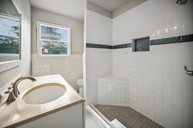 bathroom with tiled shower, vanity, tile walls, and toilet