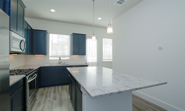 kitchen with a kitchen island, stainless steel appliances, hanging light fixtures, and light hardwood / wood-style flooring