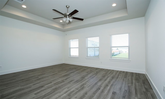 empty room featuring a tray ceiling, a wealth of natural light, ceiling fan, and dark wood-type flooring