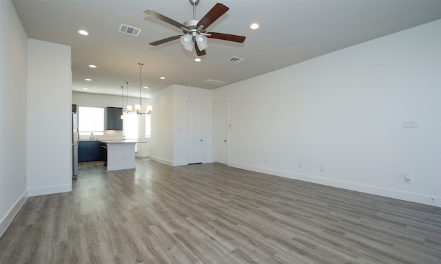 unfurnished living room featuring wood-type flooring and ceiling fan with notable chandelier