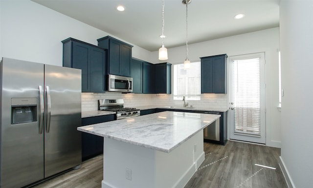 kitchen featuring appliances with stainless steel finishes, a center island, decorative light fixtures, and dark hardwood / wood-style flooring