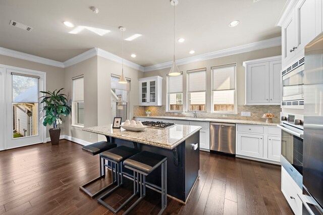 kitchen with white cabinets, a breakfast bar area, decorative light fixtures, a kitchen island, and stainless steel appliances