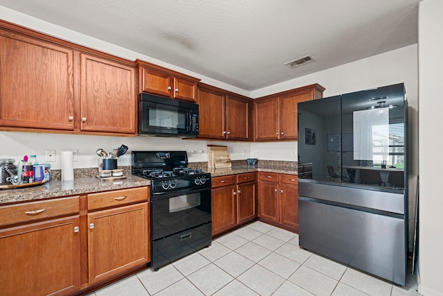 kitchen with light tile patterned floors, a textured ceiling, dark stone countertops, and black appliances