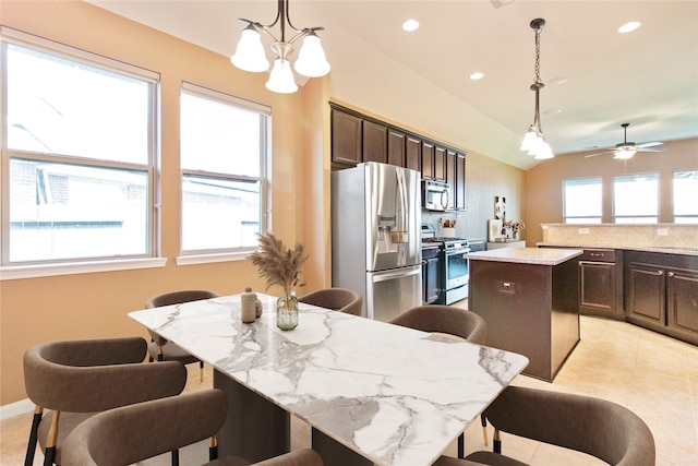 kitchen with a center island, lofted ceiling, hanging light fixtures, appliances with stainless steel finishes, and light stone counters