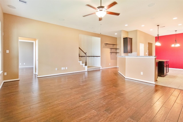 unfurnished living room featuring ceiling fan with notable chandelier and light wood-type flooring