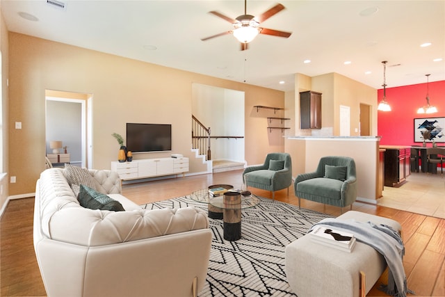 living room featuring ceiling fan with notable chandelier and light hardwood / wood-style flooring