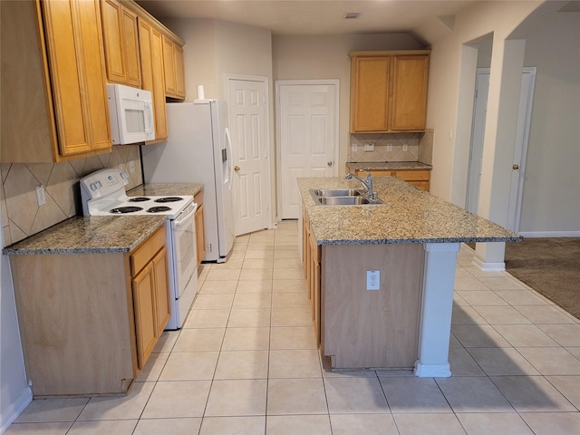 kitchen featuring sink, a kitchen island with sink, light stone counters, white appliances, and decorative backsplash