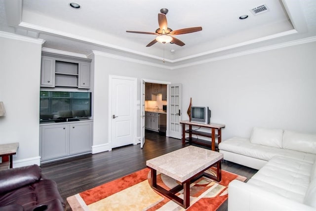 living room with a tray ceiling, ceiling fan, dark hardwood / wood-style floors, and ornamental molding