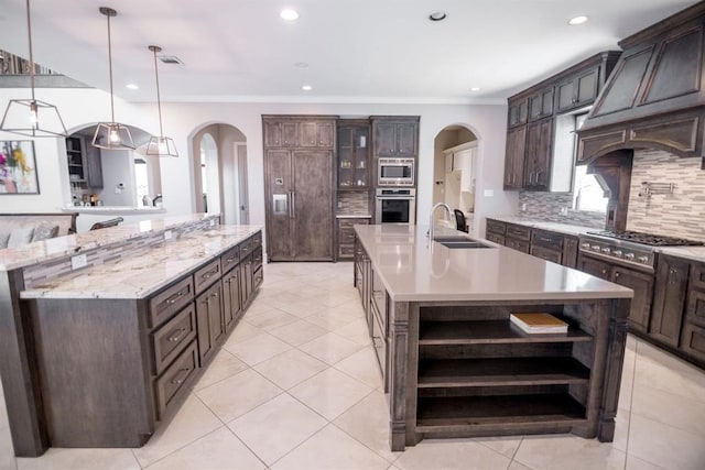 kitchen with appliances with stainless steel finishes, dark brown cabinets, sink, a large island with sink, and pendant lighting