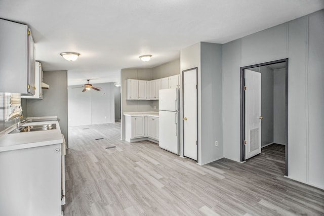 kitchen featuring light wood-type flooring, ceiling fan, sink, white fridge, and white cabinetry