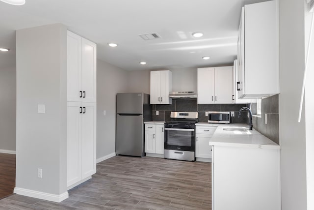 kitchen with sink, light wood-type flooring, range hood, appliances with stainless steel finishes, and white cabinetry