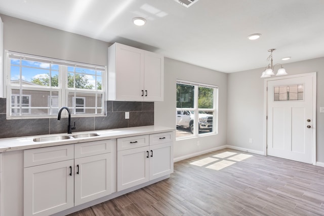 kitchen with white cabinetry, sink, pendant lighting, decorative backsplash, and light wood-type flooring