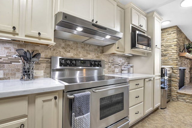 kitchen featuring decorative backsplash, light stone countertops, light tile patterned floors, appliances with stainless steel finishes, and cream cabinetry