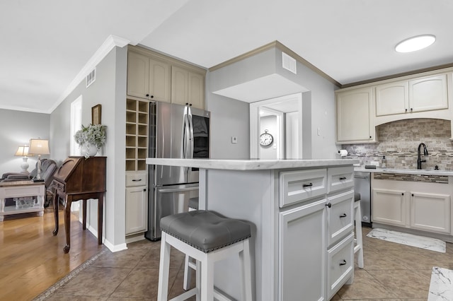 kitchen with light hardwood / wood-style flooring, backsplash, stainless steel fridge, crown molding, and a breakfast bar area